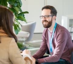 Ein shopware Mitarbeiter sitzt gegenüber von einer Frau und lächelt während eines Gespräches.
